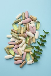 Photo of Different vitamin pills and green branch on light blue background, flat lay