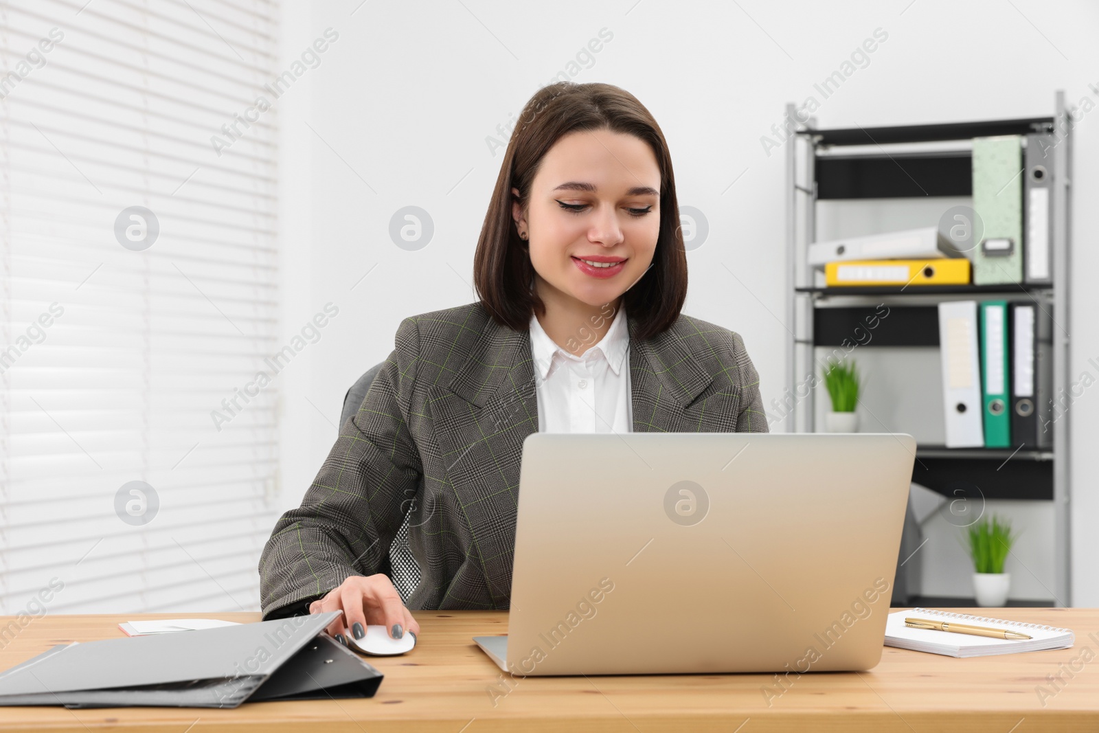 Photo of Happy young intern working with laptop at table in modern office