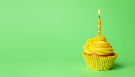 Delicious birthday cupcake with yellow cream and burning candle on green background. Space for text