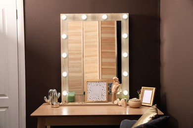 Stylish dressing table with mirror near brown wall in room