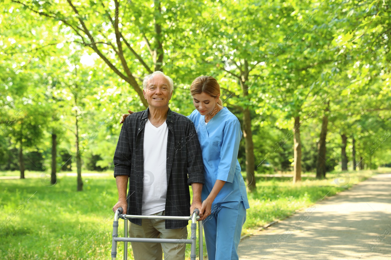 Photo of Happy nurse assisting elderly man with walking frame at park
