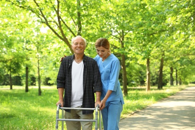 Photo of Happy nurse assisting elderly man with walking frame at park