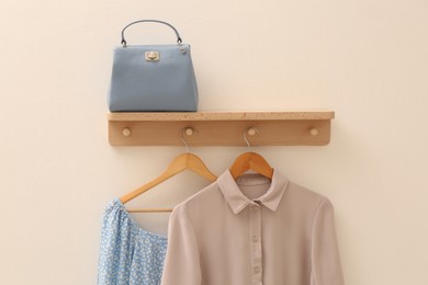 Photo of Wooden shelf with fashionable clothes and bag on beige wall. Interior element