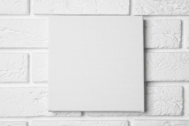 Blank canvas hanging on white brick wall, space for text