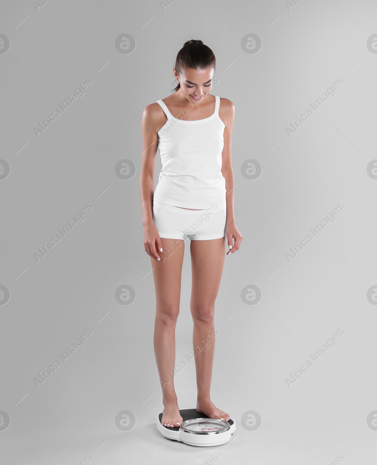 Photo of Happy young woman measuring her weight using scales on color background. Weight loss motivation