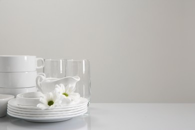 Photo of Set of many clean dishware, flowers and glasses on light table. Space for text