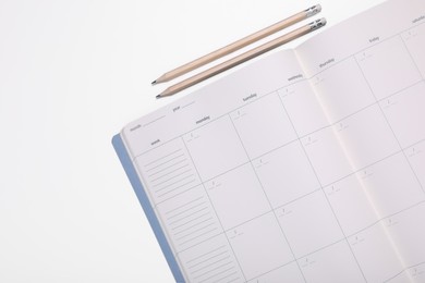 Open monthly planner and pencils on white background, top view. Space for text