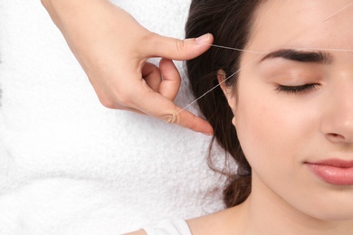 Photo of Young woman having professional eyebrow correction procedure in beauty salon, closeup