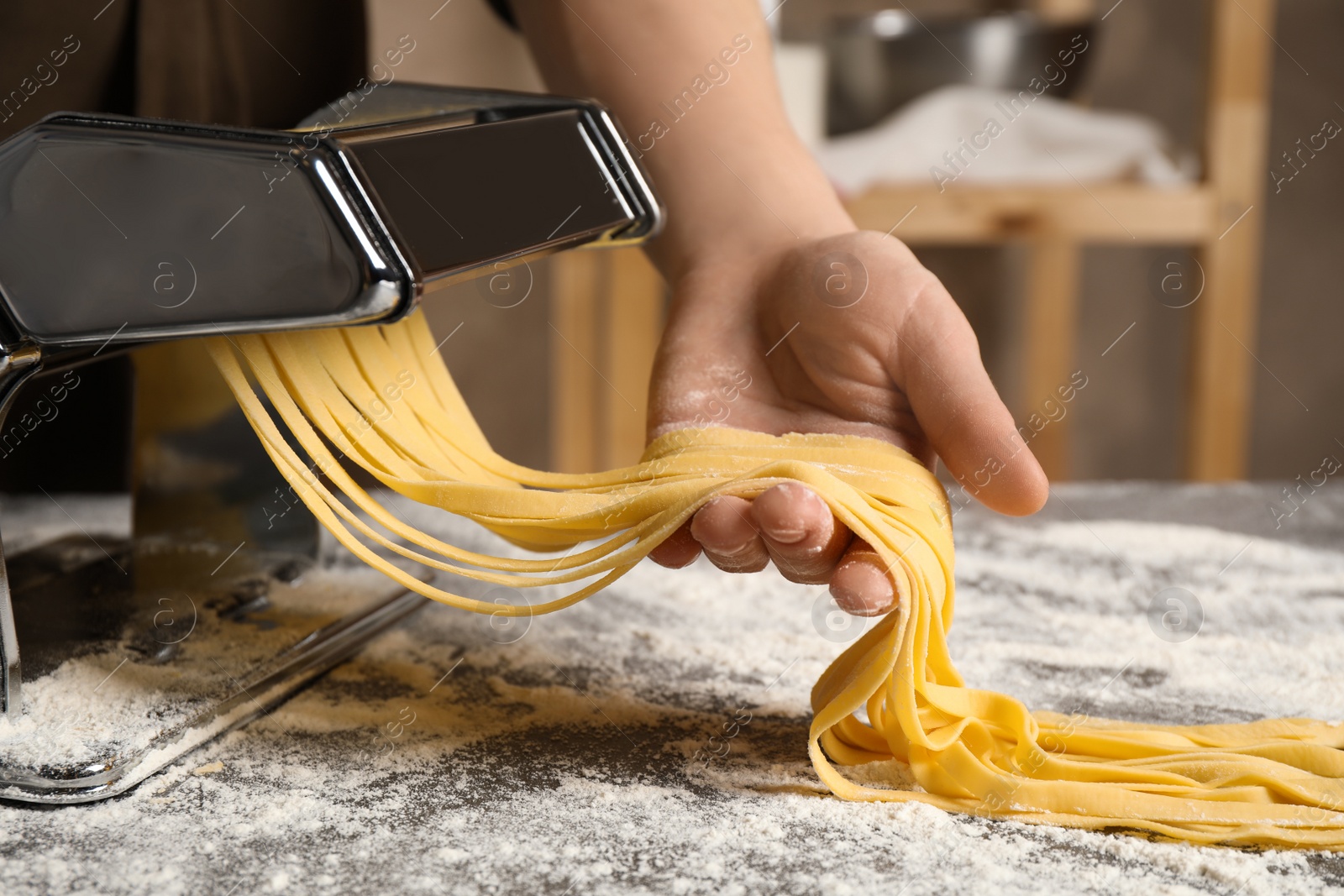 Photo of Woman preparing noodles with pasta maker machine at table indoors, closeup