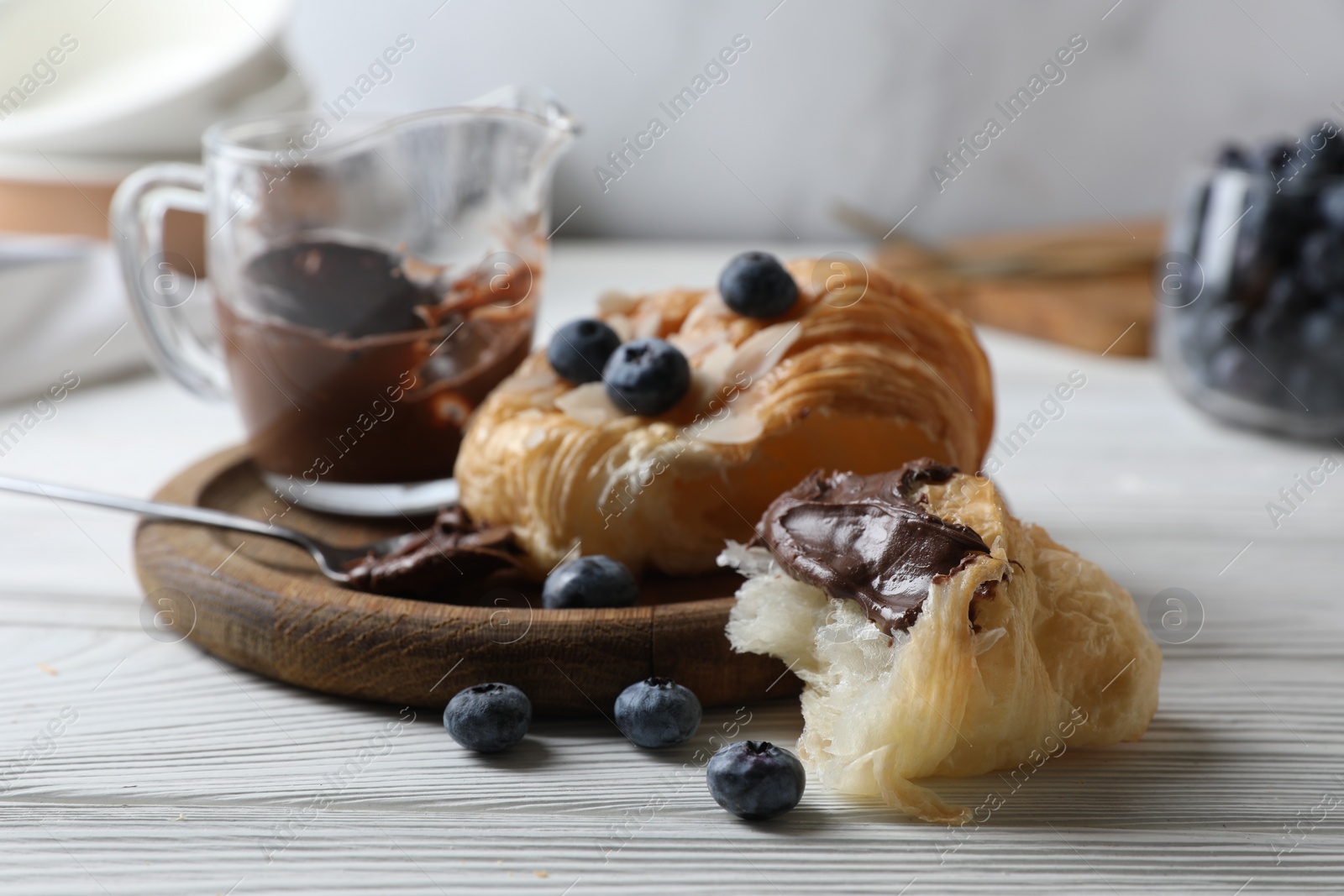 Photo of Delicious croissant with chocolate and blueberries on white wooden table, closeup