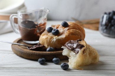 Photo of Delicious croissant with chocolate and blueberries on white wooden table, closeup