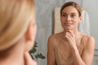 Woman massaging her face near mirror in bathroom