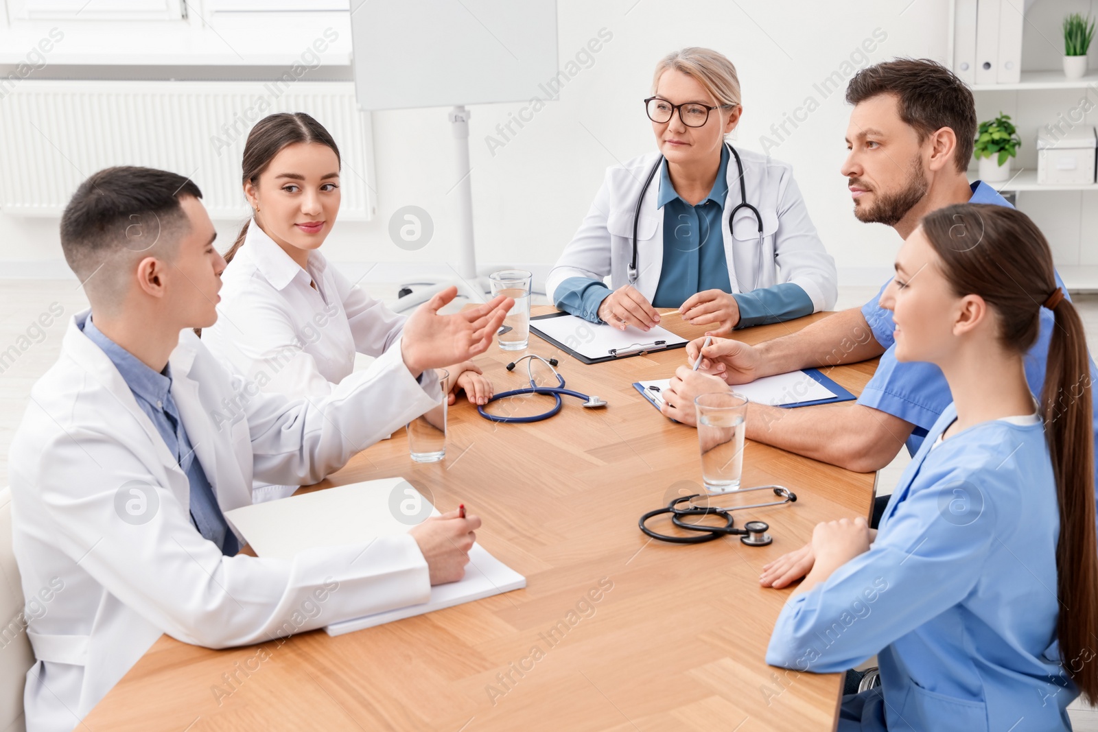 Photo of Medical conference. Team of doctors having discussion at wooden table in clinic