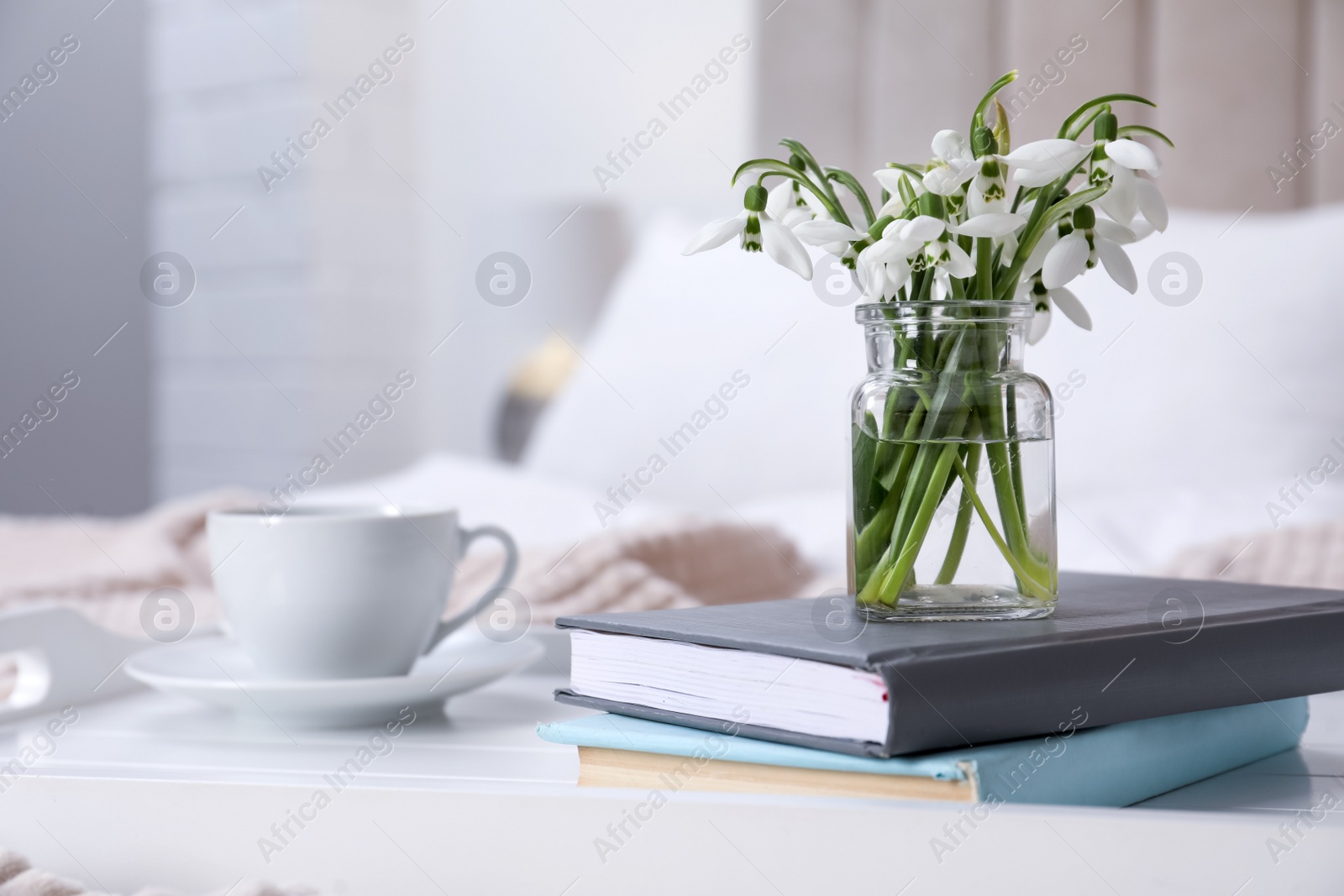 Photo of Beautiful snowdrops, books and cup of coffee on tray in bedroom. Space for text
