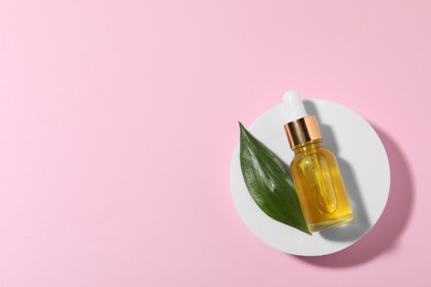 Photo of Bottle of cosmetic oil and green leaf on pink background, top view. Space for text