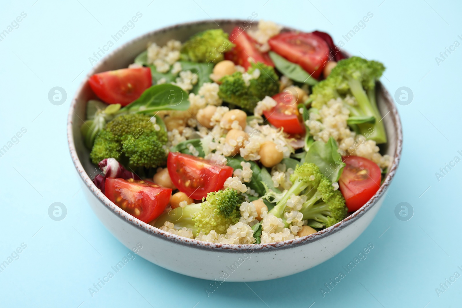 Photo of Healthy meal. Tasty salad with quinoa, chickpeas and vegetables on light blue table, closeup