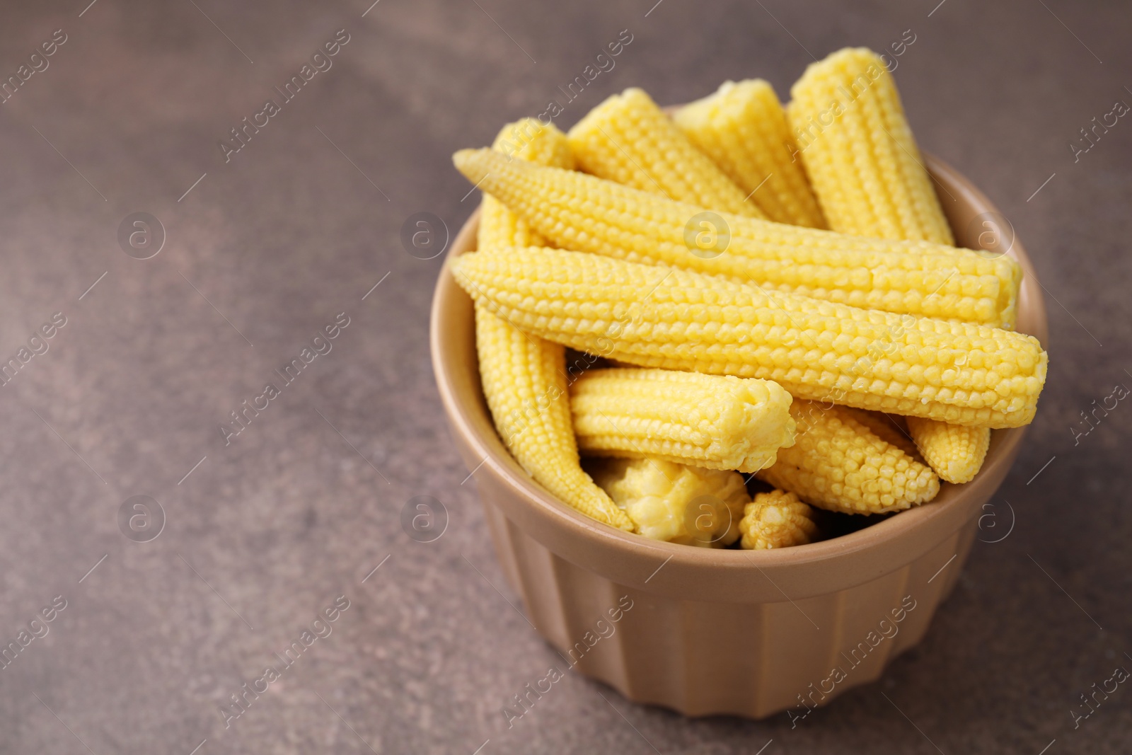 Photo of Tasty fresh yellow baby corns in bowl on brown table, closeup. Space for text