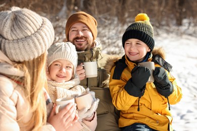 Photo of Happy family warming themselves with hot tea outdoors on snowy day