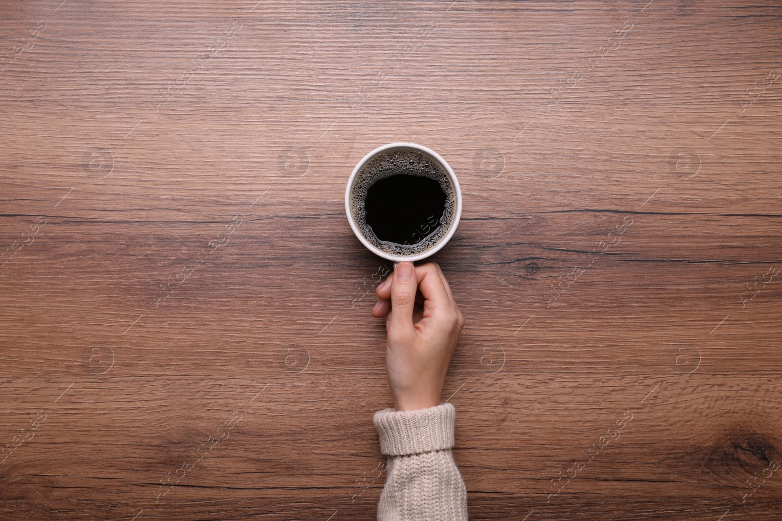 Photo of Woman with cup of coffee at wooden table, top view