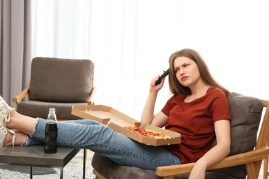 Lazy young woman with pizza and drink watching TV at home