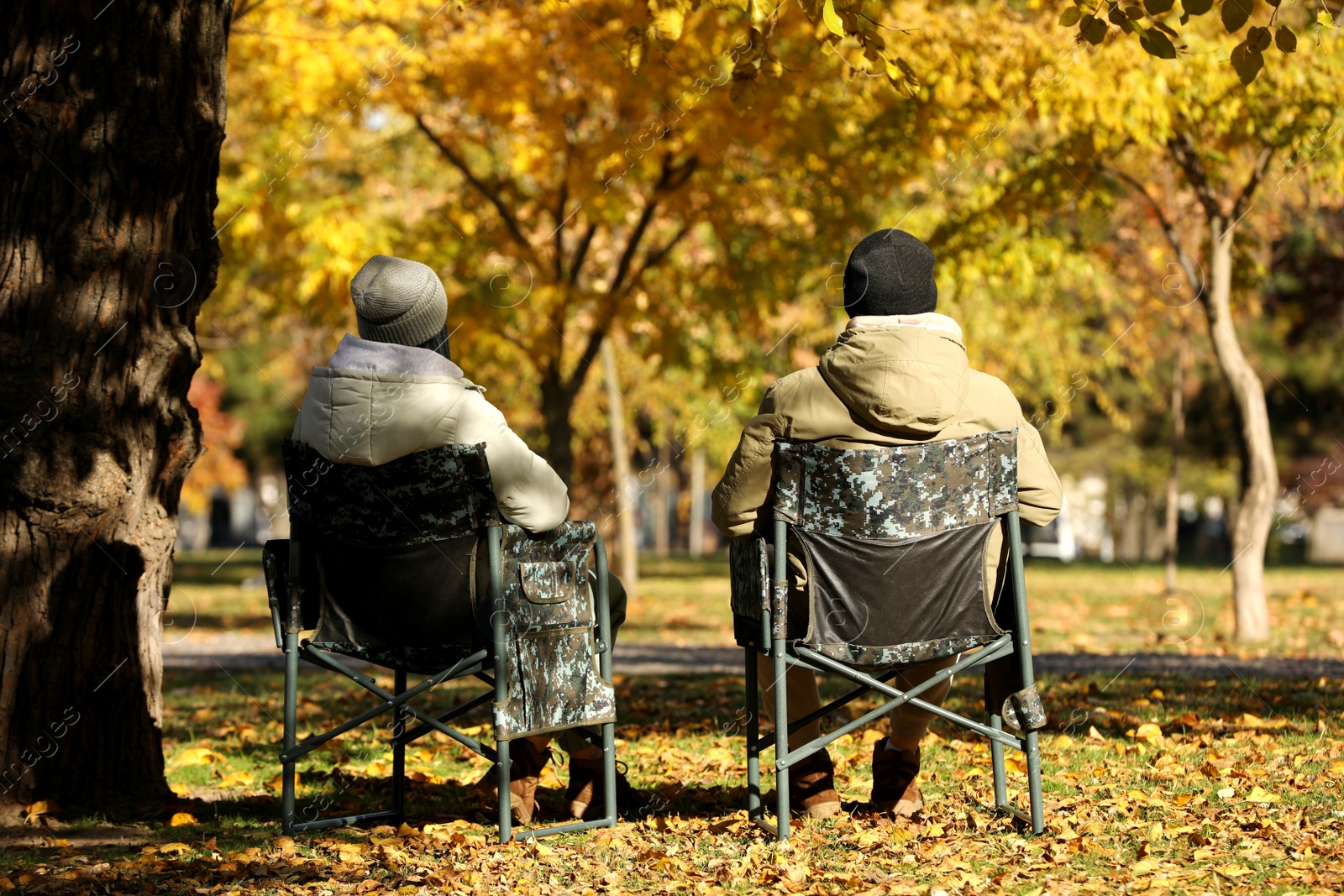 Photo of Couple sitting in camping chairs outdoors on autumn sunny day, back view