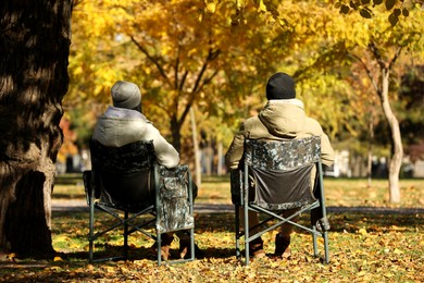 Couple sitting in camping chairs outdoors on autumn sunny day, back view