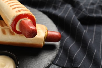 Tasty french hot dogs with different sauces on slate plate, closeup. Space for text