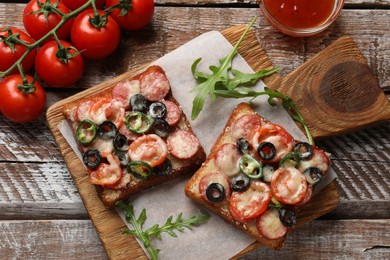 Tasty pizza toasts, sauce, tomatoes and arugula on wooden table, top view