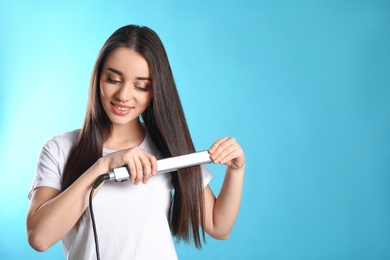 Happy woman using hair iron on color background. Space for text