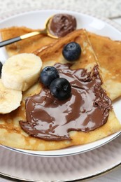 Photo of Tasty crepes with chocolate paste, blueberries and banana served on white wooden table, closeup