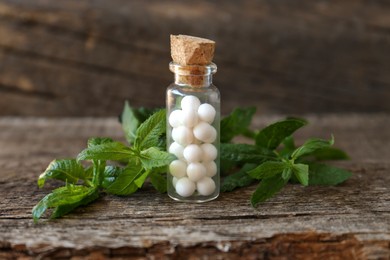 Photo of Bottle with homeopathic remedy and mint on wooden table