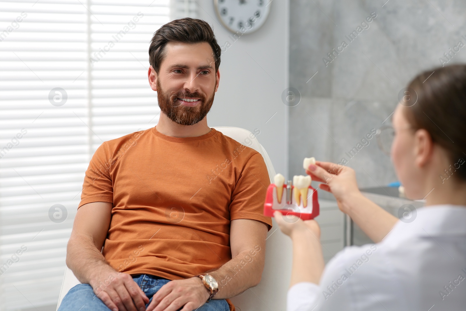 Photo of Doctor with educational model of dental implant consulting patient in clinic