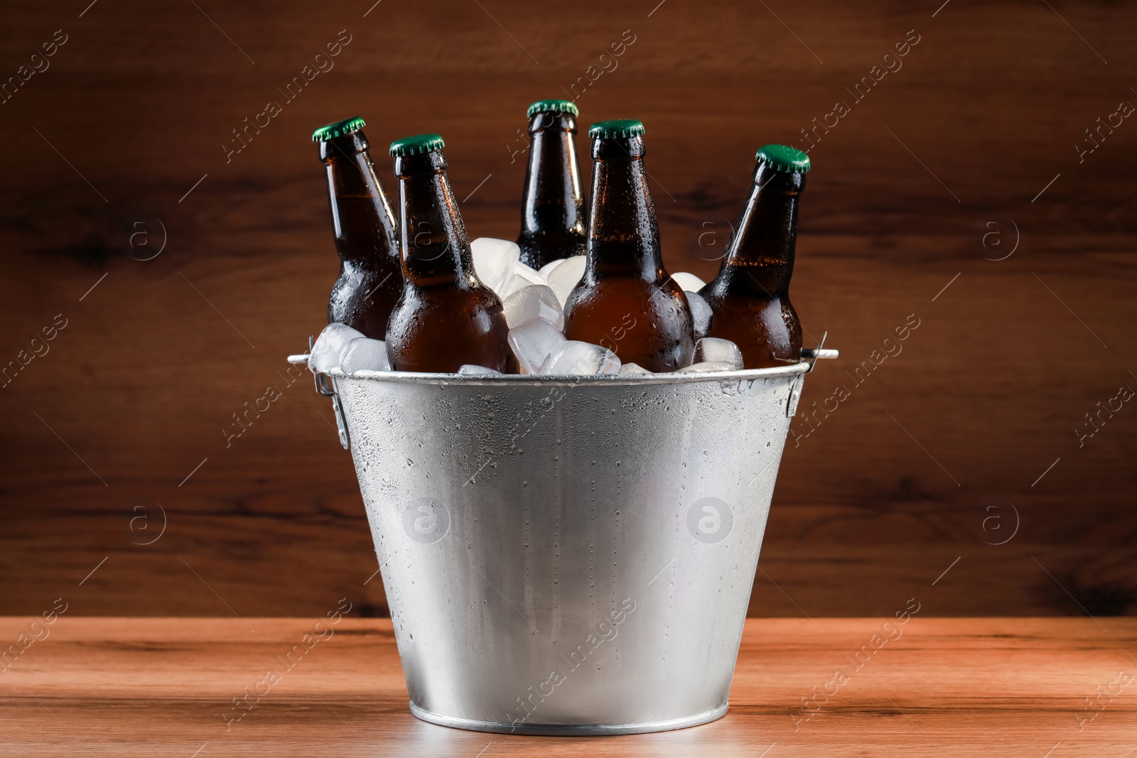 Photo of Metal bucket with bottles of beer and ice cubes on wooden table