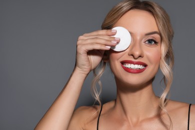 Photo of Smiling woman removing makeup with cotton pad on dark grey background, closeup. Space for text