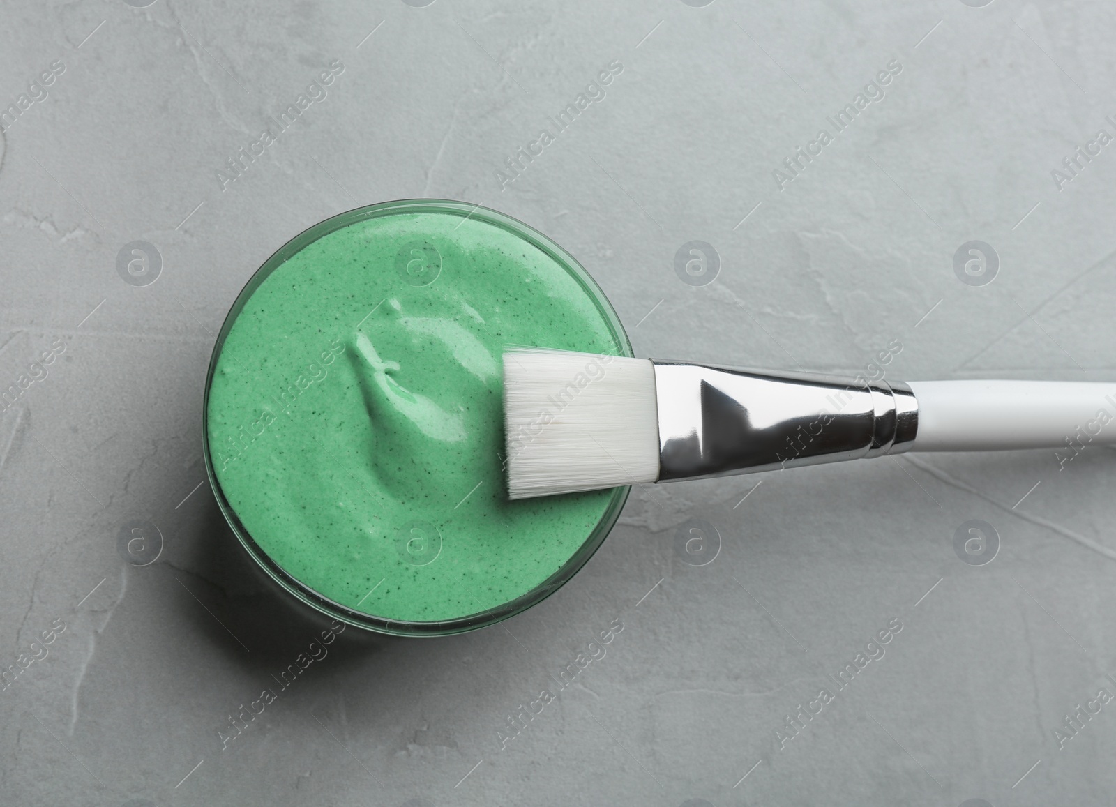 Photo of Freshly made spirulina facial mask in bowl and brush on light grey background, top view