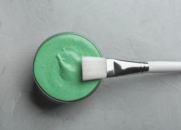 Photo of Freshly made spirulina facial mask in bowl and brush on light grey background, top view
