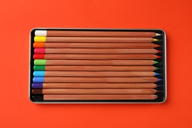 Photo of Box with many colorful pastel pencils on orange background, top view. Drawing supplies