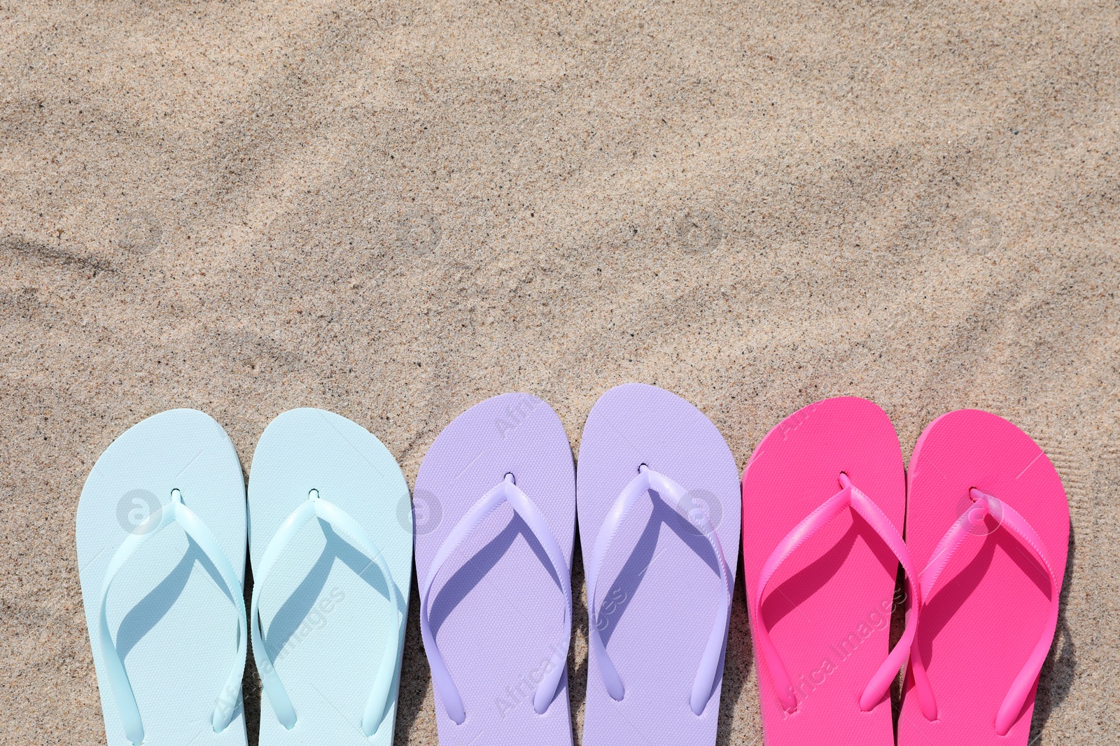 Photo of Stylish colorful flip flops on sand outdoors, flat lay. Space for text