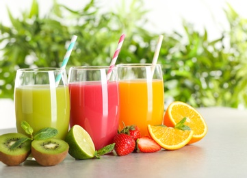 Photo of Glasses of different juices with straws and fresh fruits on table against blurred background. Space for text