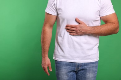 Man suffering from stomach pain on green background, closeup and space for text