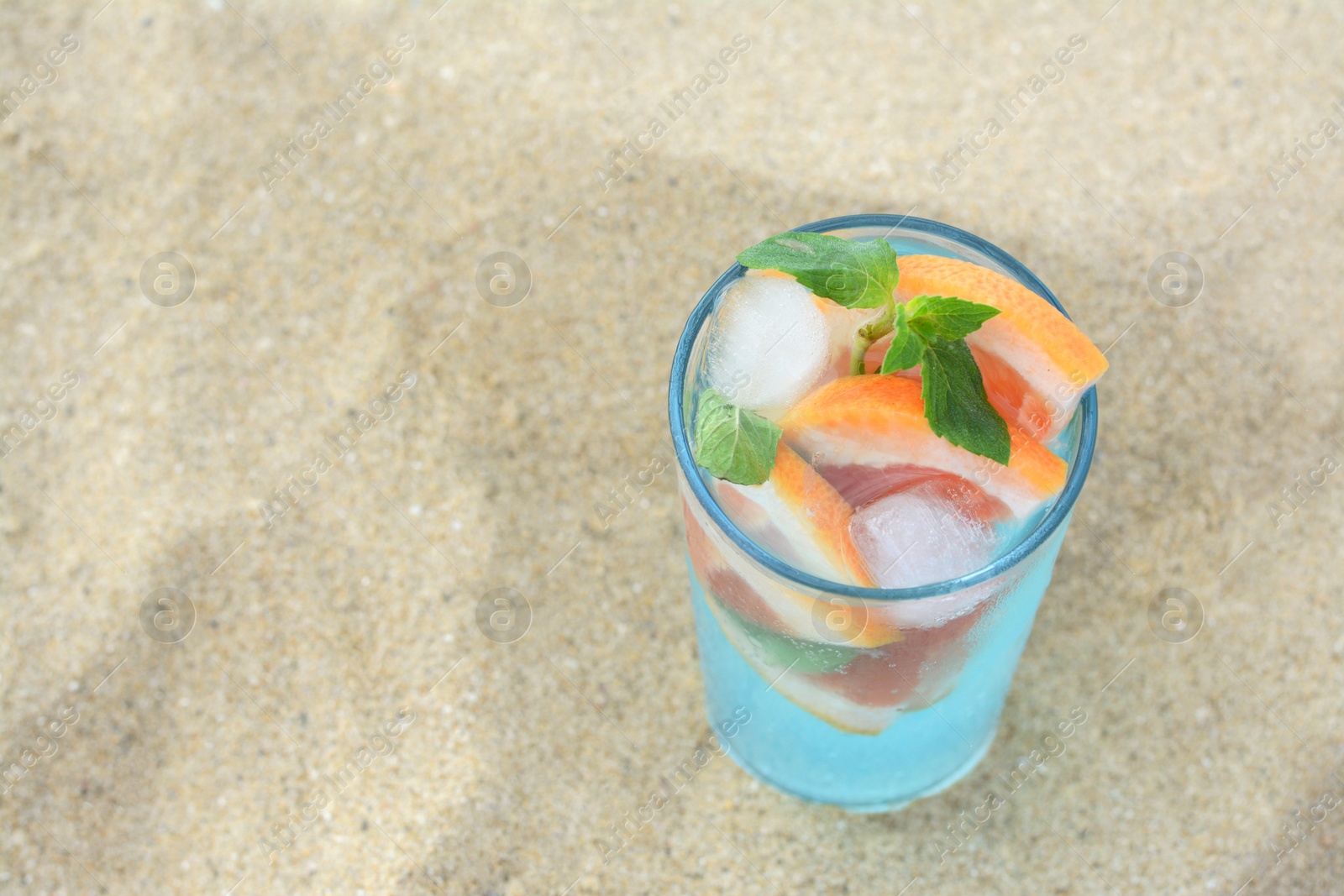 Photo of Glass of refreshing drink with grapefruit and mint on sandy beach, above view. Space for text