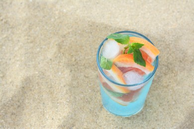 Glass of refreshing drink with grapefruit and mint on sandy beach, above view. Space for text