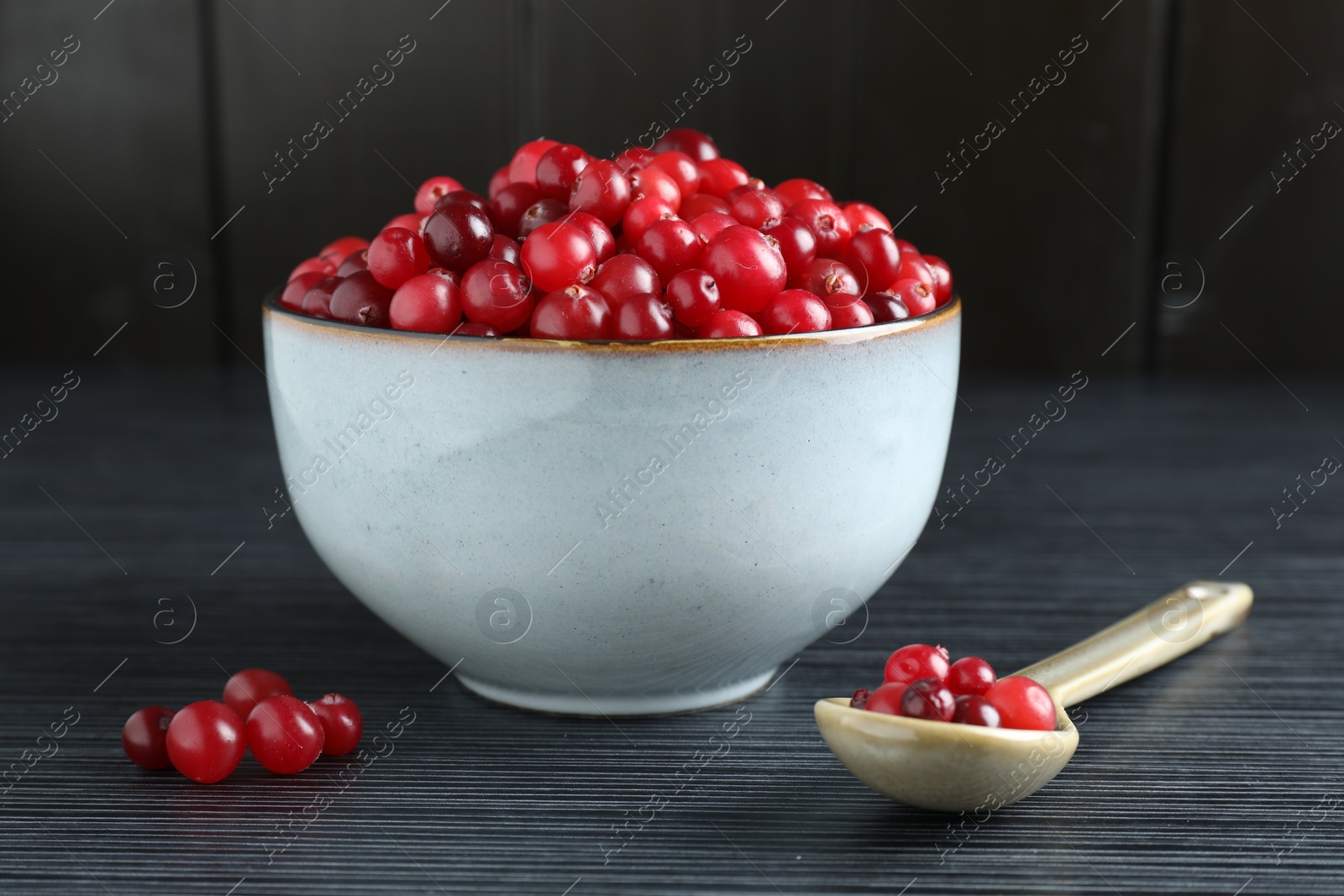 Photo of Cranberries in bowl and spoon on black wooden table, closeup