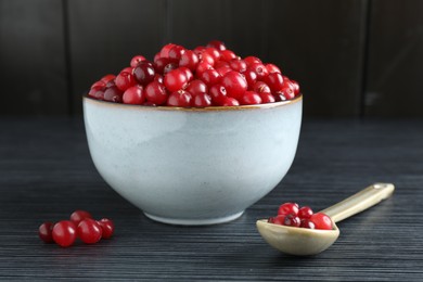 Photo of Cranberries in bowl and spoon on black wooden table, closeup