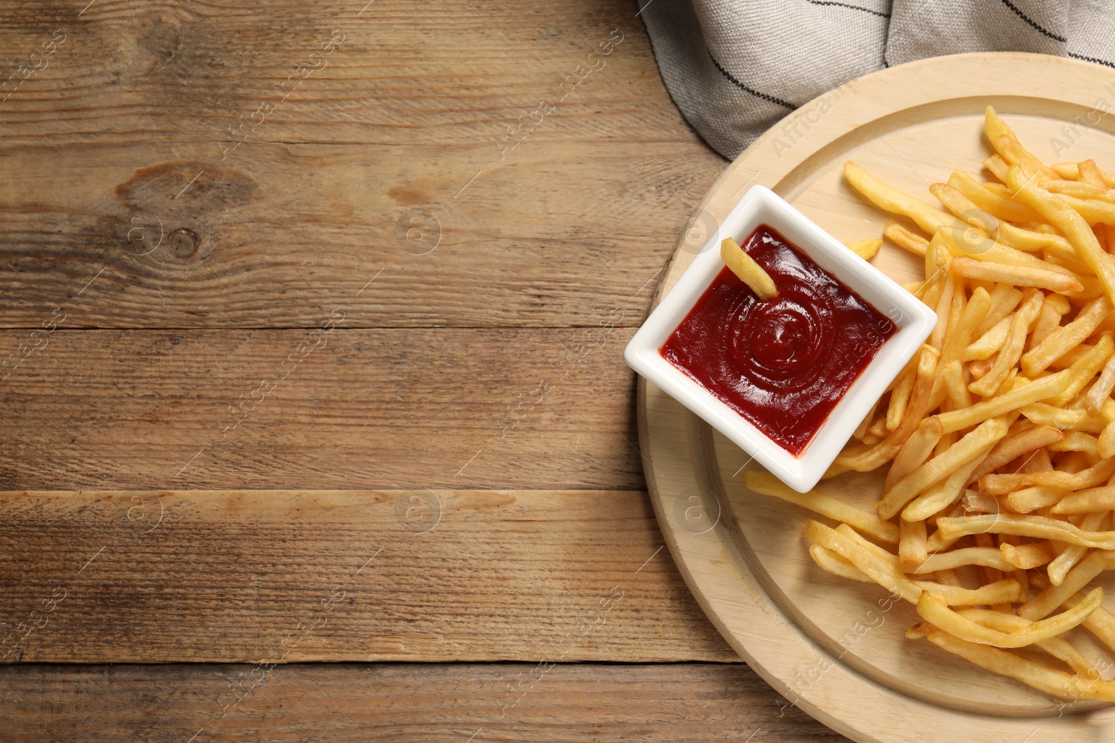 Photo of Board with tasty ketchup and fries on wooden table, top view. Space for text
