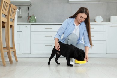 Photo of Beautiful young woman feeding her adorable Pug dog in kitchen, space for text