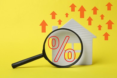 Image of Mortgage rate rising illustrated by upward arrows and percent sign. House model and magnifying glass on yellow background