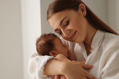 Mother holding her cute newborn baby indoors. Space for text