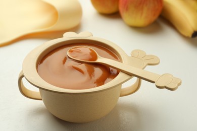 Photo of Bowl and spoon with tasty pureed baby food on white table, closeup