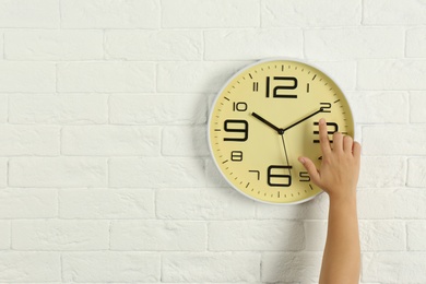Woman touching clock on white brick wall, space for text. Time management